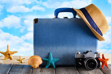 Blue suitcase for summer holidays, hipster hat; retro photo camera and shells on wooden table and...