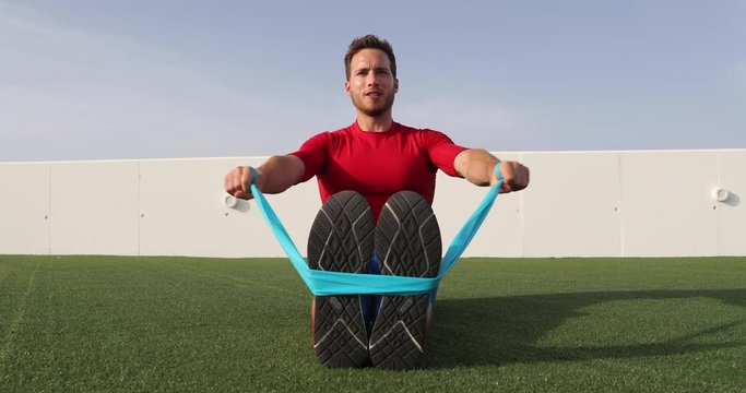 Fitness man training shoulders back and arms with resistance bands at outdoor gym. Body workout with equipment outside. Elastic rubber band accessory.