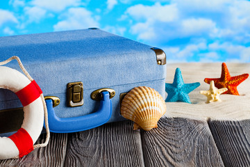 Holiday travel suitcase, lifebuoy and shells on wooden table