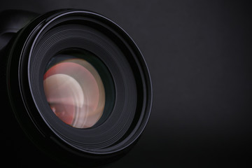 Modern camera with lens on black background, closeup. Space for text