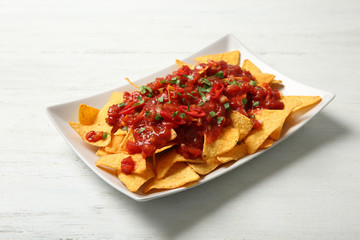 Plate of delicious mexican nachos chips with salsa sauce on white wooden table