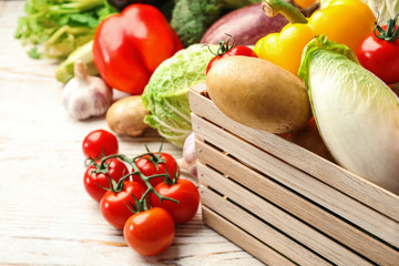 Fresh vegetables and wooden crate on white table, closeup