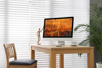 Modern PC on table near window with blinds in room