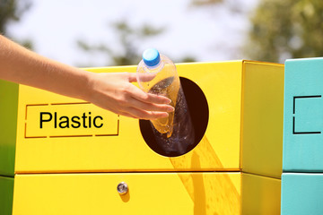 Woman throwing plastic bottle into sorting bin on city street, closeup. Recycling waste