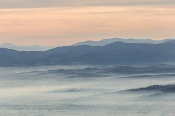 Fototapeta na wymiar Fog filling a valley in Umbria (Italy) at dawn, with layers of mountains and hills and various shades of blue