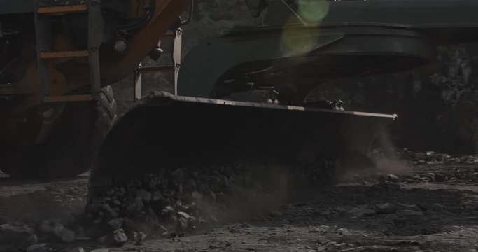 Slow motion close-up Motor Grader machine flattening and leveling gravel sub layer of surfacing new road. Construction machine with long blade used to create flat surface during grading on dirt roads