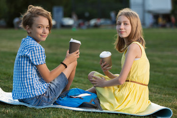 teenagers a boy and a girl on a green lawn, sit on a mat and hold cardboard cups of coffee, a date or a joint outdoor recreation, lifestyle