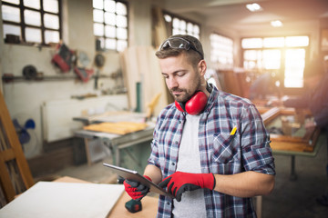 Young professional worker carpenter with protective glasses holding tablet computer and checking...