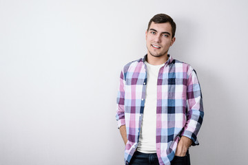 Fototapeta premium Portrait of modern European young man in pink plaid shirt and white t-shirt against gray wall