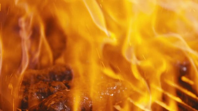 Slow motion close up of traditional Balkan cevapi minced meat sausages cooking on a charcoal grill with orange flames bursting.
