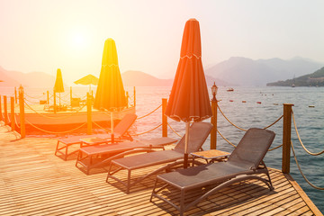 Wooden pier with sunbeds and parasols on the background of sea and mountains