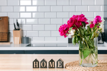 Beautiful pink peonies in a glass vase standing on the kithcen with white brick tile wall.