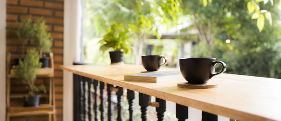 Black coffee cup with a book on light wooden bar at home in the morning with green and natural view.