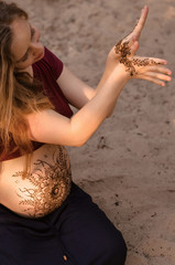 Pregnant woman with mehendi henna tattoo on her belly and hands, cropped image. Motherhood concept, happy maternity