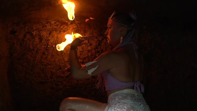 The girl in the cave is dancing dangerously with fire in her hands.