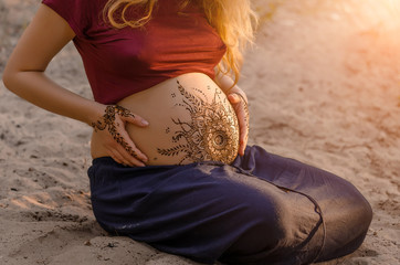 Pregnant woman with mehendi henna tattoo on her belly and hands, cropped image, hands on pregnant...