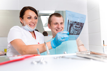 Obraz premium People, medicine, stomatology, technology and health care concept - happy female dentist with teeth x-ray on tablet pc computer and patient girl at dental clinic office