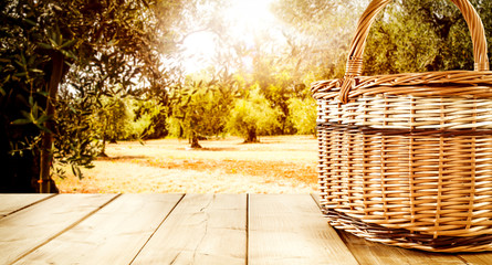 Wooden table background with a picnic basket and autumn orchard view in distance. Empty space for...