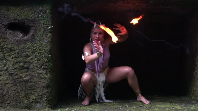 The girl in the cave is dancing dangerously with fire in her hands.