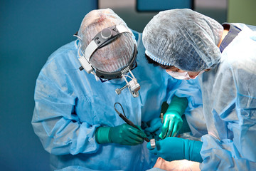 Surgeon and his assistant performing cosmetic surgery on nose in hospital operating room. Nose reshaping, augmentation. Rhinoplasty.