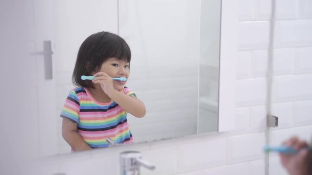 asian little girl brushes her teeth alone in the bathroom before go to bed