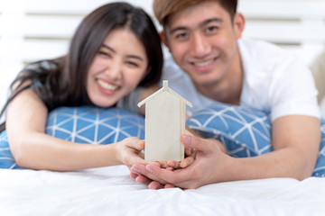 Young couple holding house toy on the bed