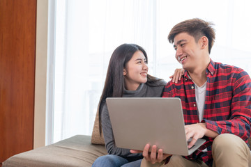 Asian young woman and handsome man sitting on couch, They happily to use smartphone together, copy space