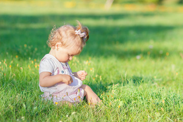 Fototapeta premium Cute little girl sits on the green grass, outdoors, summer time, blurred background