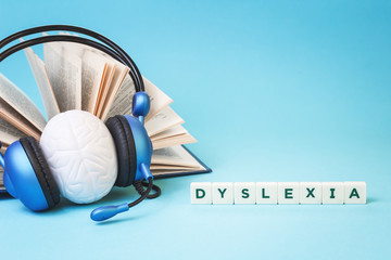 Dyslexia word with an open book and brain stress relief in headphones on blue background, reading difficulty and disorder and auditory memory concept. Education and neurology with copy space