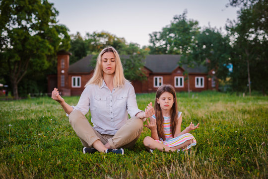 Mother and daughter child meditate together in Lotus position outdoors.