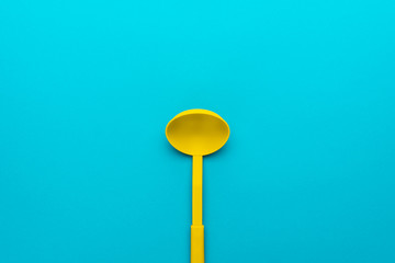Top view photo of vivid plastic kitchen utensil. Minimalist flat lay image of yellow ladle over turquoise blue background with copy space. Central composition of dipper on blue table.
