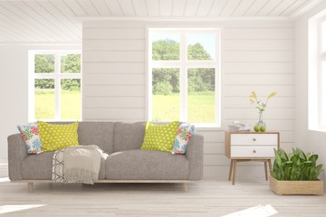 Stylish room in white color with sofa and summer landscape in window. Scandinavian interior design. 3D illustration