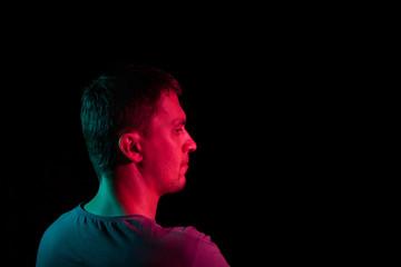Close-up of the face of an unshaven face of a caucasian man looking away with stubble in the dark, illuminated on one side in Blue and on the other red on a black isolated background. Cyberpunk style