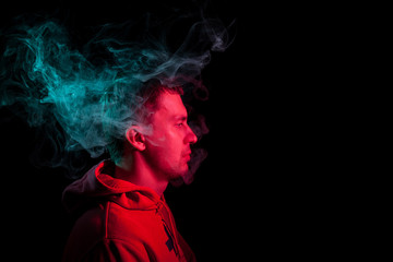 Portrait of a man in profile face looking on a black isolated background with a feeling of sadness and loneliness, around the head a cloud of green and red smoke. The soul and feelings.