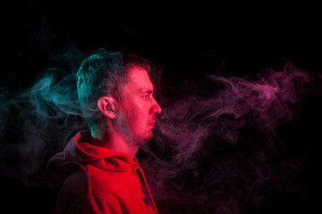 Portrait of a man in profile face looking on a black isolated background with a feeling of sadness and loneliness, around the head a cloud of green and pink smoke. The soul and feelings.