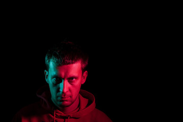 Close up portrait of the face of an adult serious man look frowningly: straight nose, expressive eyes, ears, beard; illuminated with blue and red colored light on a black background.