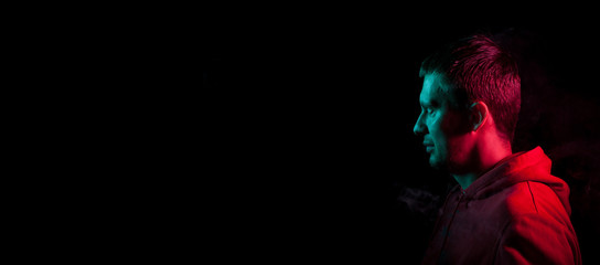 Close-up of the face of an unshaven face of a caucasian man looking away with stubble in the dark, illuminated on one side in Blue and on the other pink on a black isolated background. Cyberpunk style