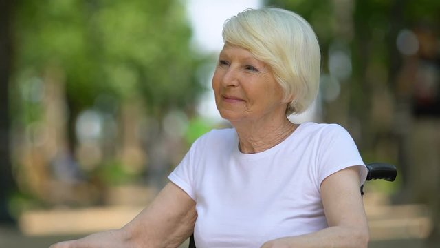 Cheerful disabled woman sitting in park and breathing fresh air, rehabilitation