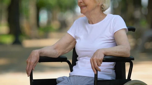 Mature woman sitting in wheelchair on hospital territory, rehabilitation