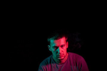 Portrait of a man in profile face on a black isolated background with a feeling of sadness and loneliness, around the head a cloud of blue and pink smoke. The soul and feelings.
