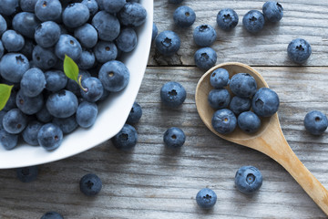 Appetizing fresh blueberries in white ceramic bowl with wooden background