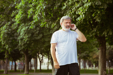 Senior man as runner with fitness tracker at the city's street. Caucasian male model using gadgets while jogging and cardio training in summer's morning. Healthy lifestyle, sport, activity concept.