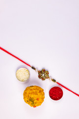 Indian Festival concept - Elegant Rakhi with rice grains and kumkum in a flat tin box and sweets on a white surface. A traditional rakhi showing the bond between brother and sister