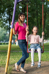 Mom with her daughter on a swing in the park.