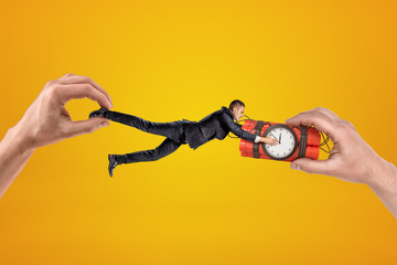 Two hands, holding small businessman who is clutching with his both hands at dynamite time bomb,...
