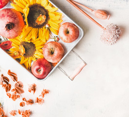 Tray with apples, sunflowers and pomegranate  on white table with autumn leaves and botanical decoration, top view. Flat lay. Modern. Minimal. Fall seasonal layout. Copy space for your design.