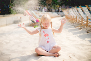 An einem sonnigen Sommertag wirft ein Mädchen am Strand Sand. Reuniting with nature. Childhood,...