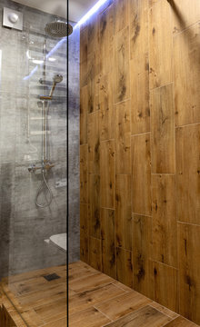 Modern glass frameless shower cubicle with wooden wall and floor in bathroom interior, copy space