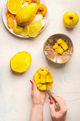 Mango preparation step by step. Female hands girl take mango cubes from the peel with a spoon on white background with fruits plate, top view.