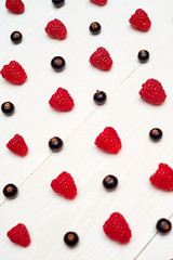 Ripe sweet raspberries and black currant on white wood background, copy space. Fresh berries. Summer and healthy food concept